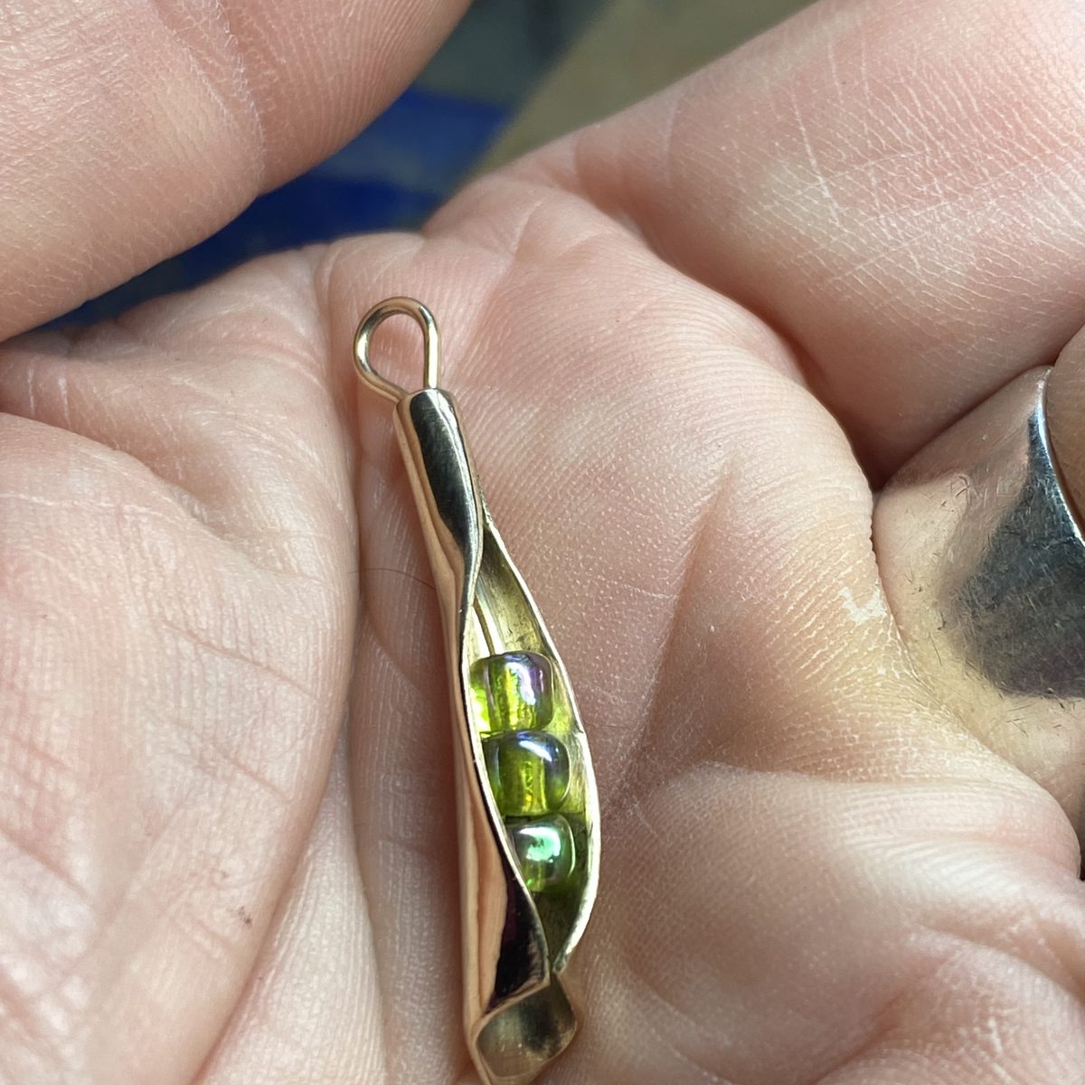 Silver pea-pod pendant holding green beads, held in a palm