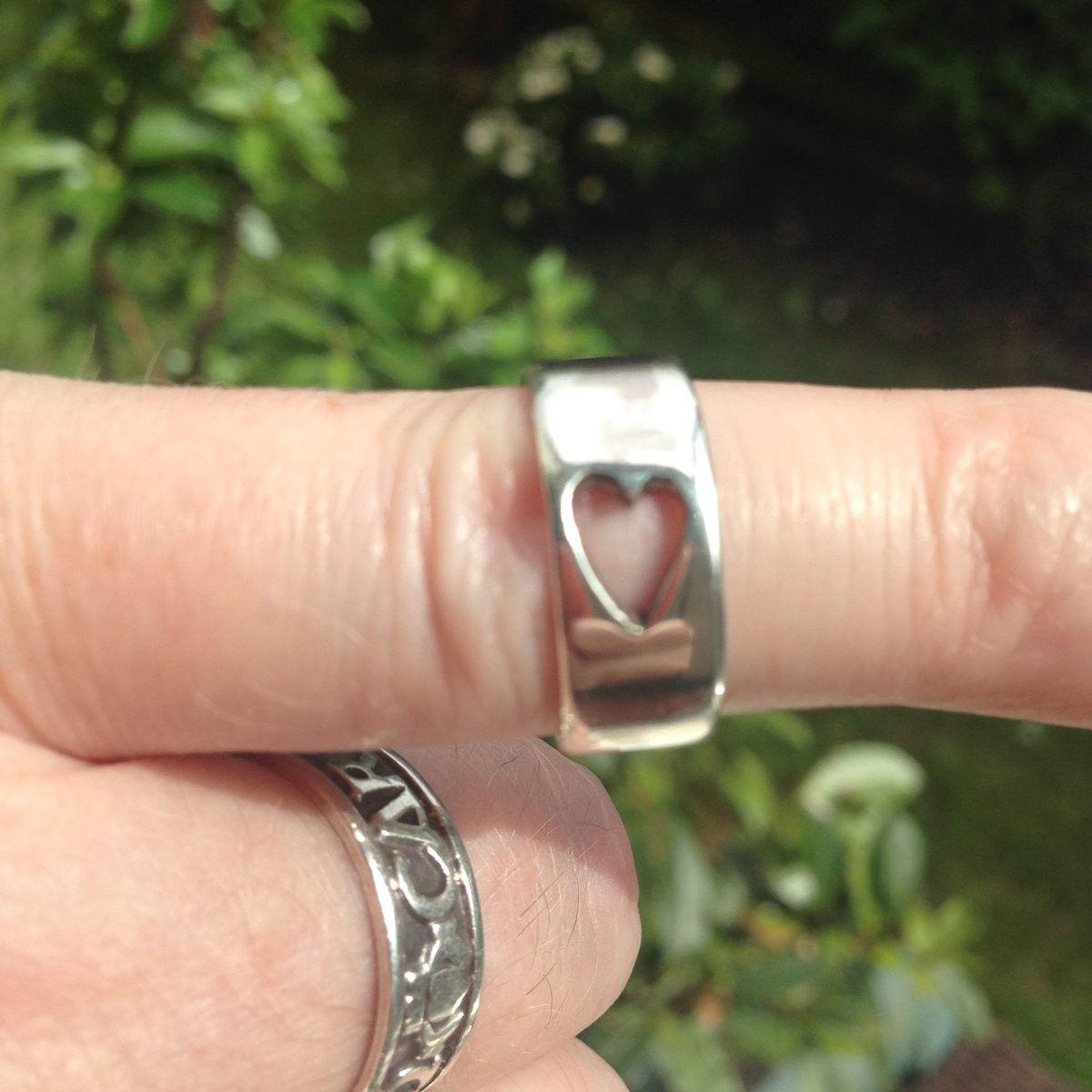 Silver band ring with a heart cut-out, worn on a finger